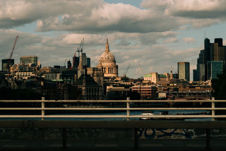 A wide-angle view of St. Paul's Cathedral in London featuring its large domed roof and classical architecture, situated on a city street with modern and historic buildings nearby. Prominent in the for